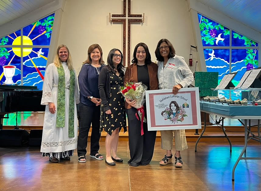 A group of four women stands in front of a church, showcasing a plaque. 