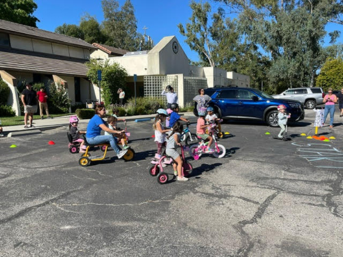 kids riding bicycle with adults watching.